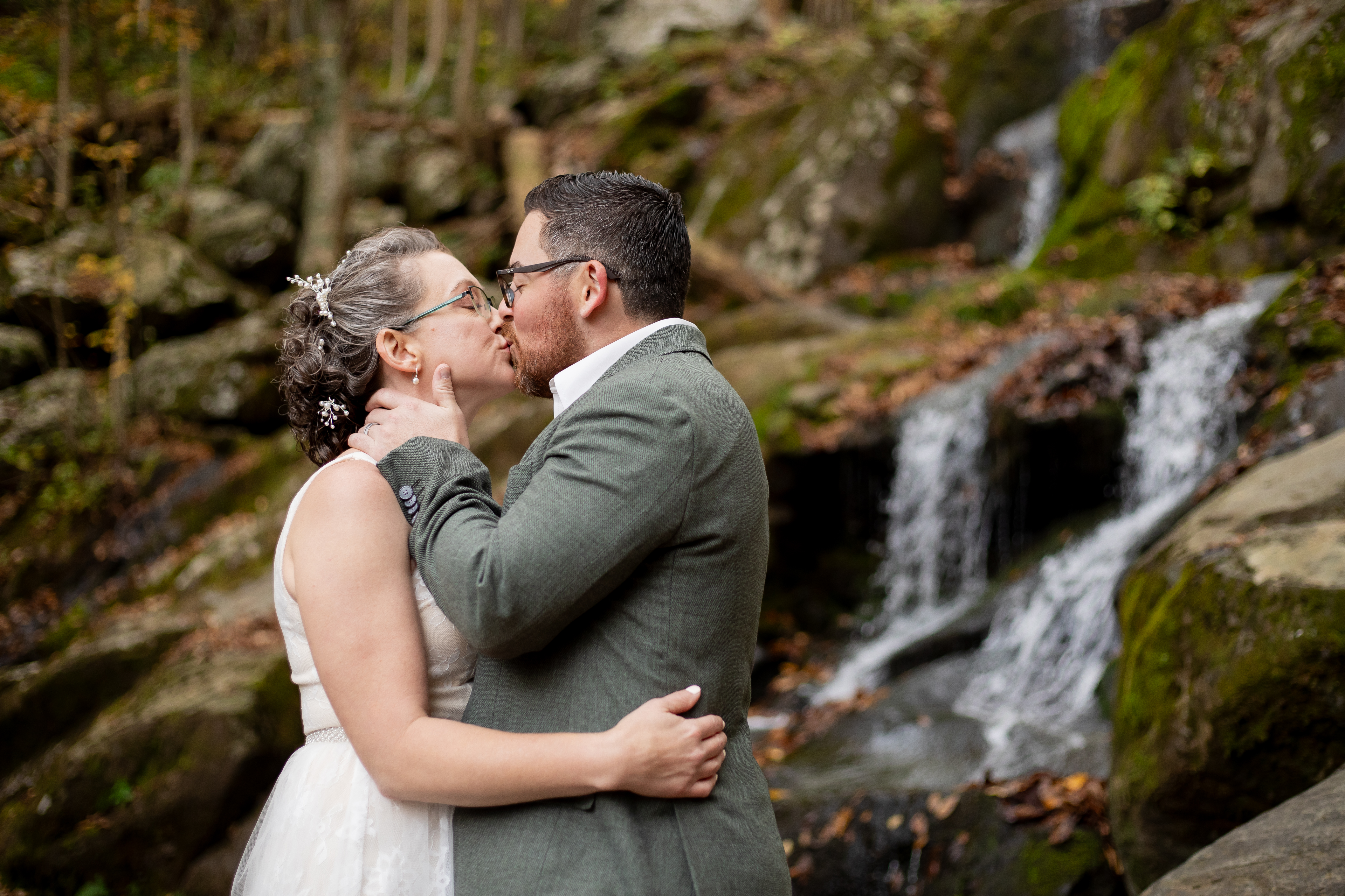 Couple kissing at Dark Hollow Falls in fall with moss-covered rocks and cascading water