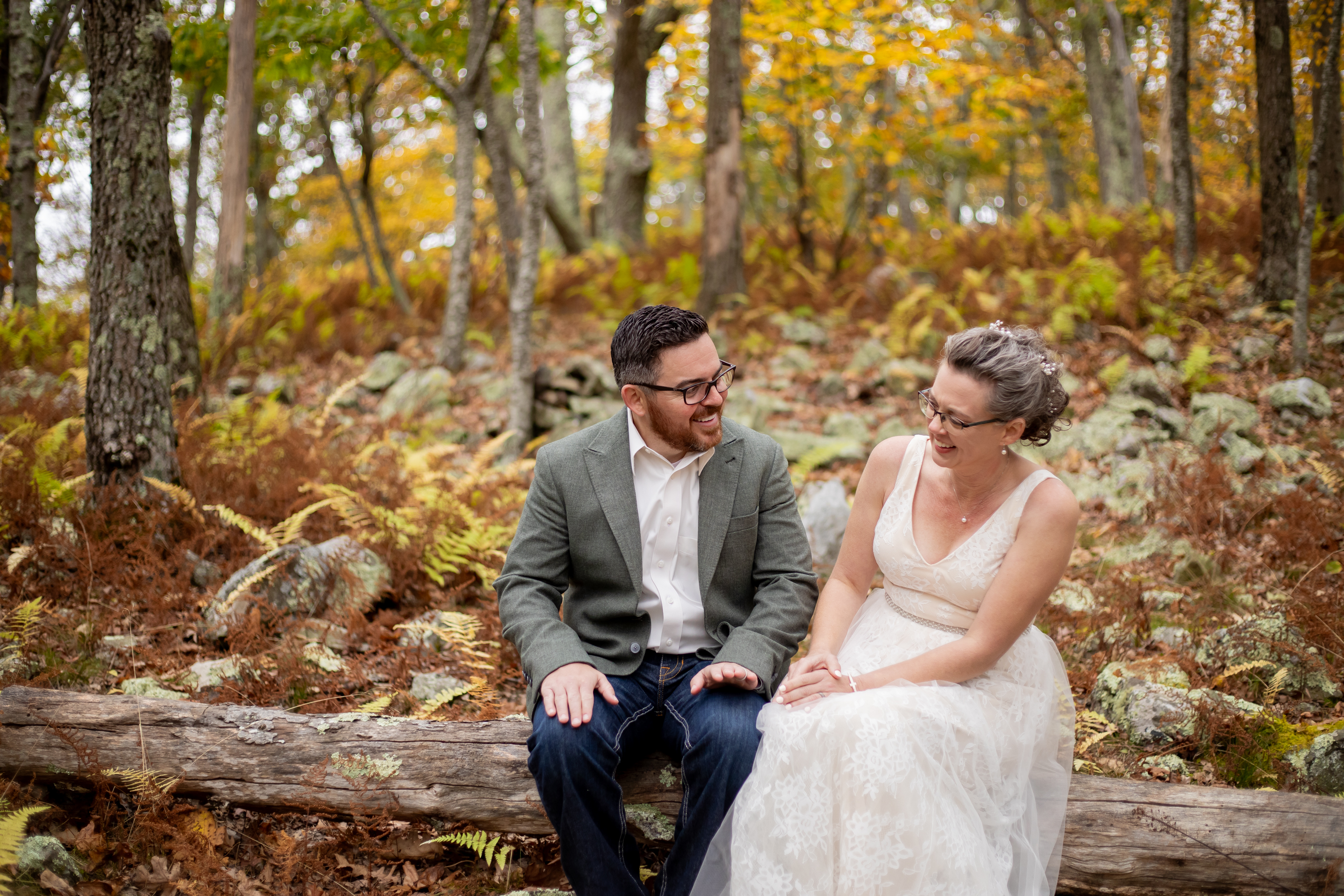 Couple laughing together on a fallen log surrounded by golden yellow fall foliage and ferns in Shenandoah National Park