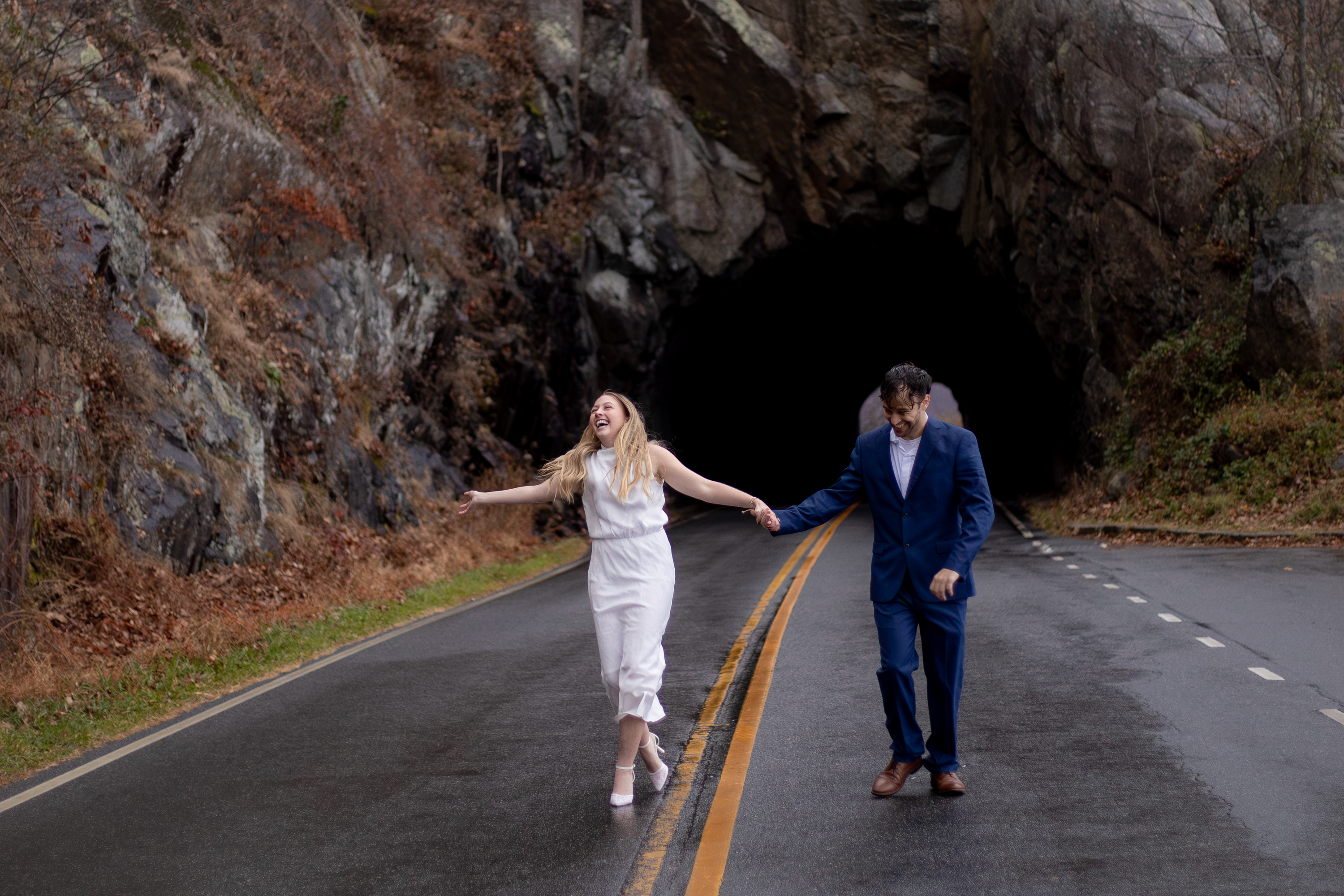 Couple laughing and walking hand in hand on a wet Skyline Drive road emerging from a tunnel, Shenandoah National Park
