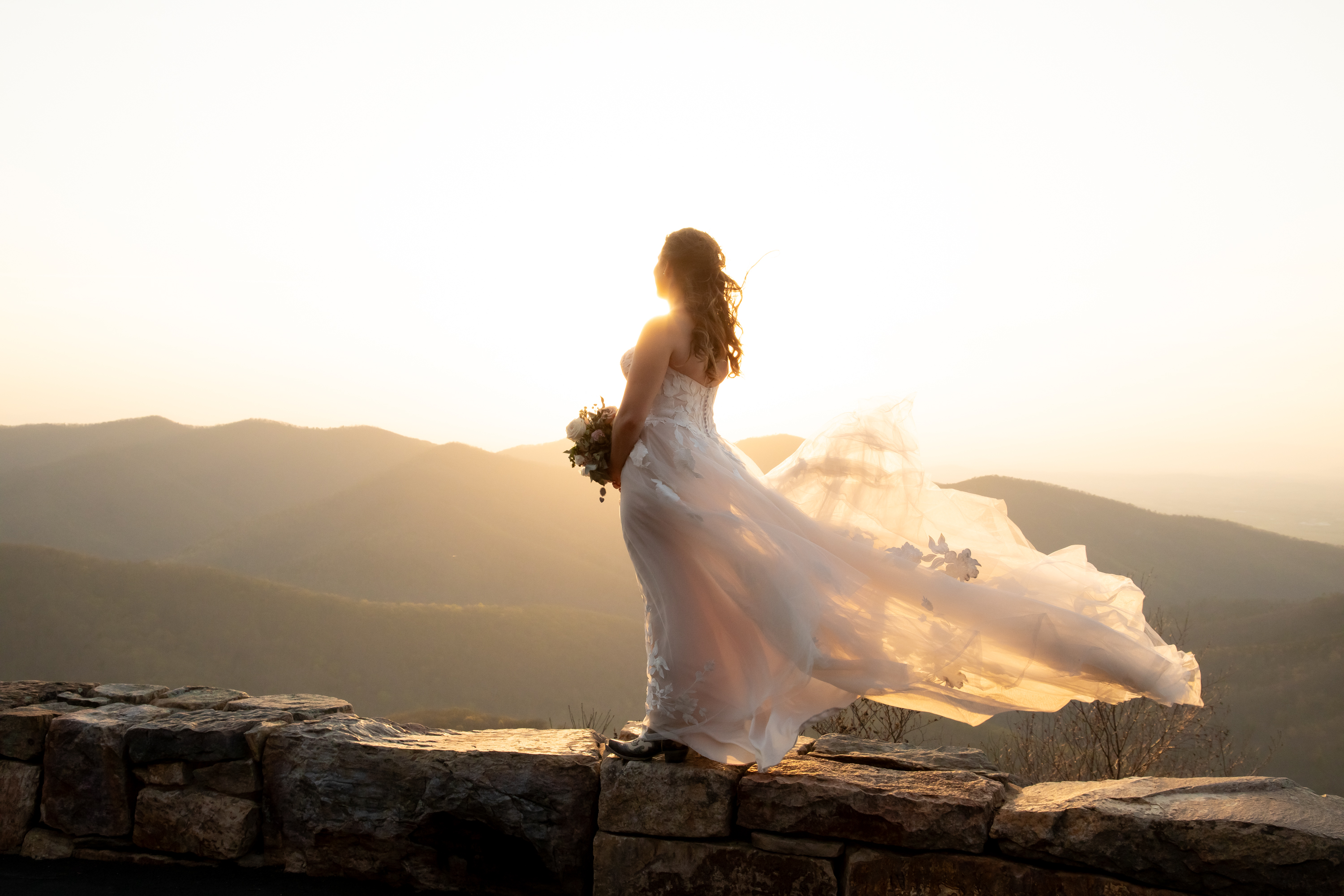 Bride in flowing white gown at a Shenandoah National Park overlook at golden hour
