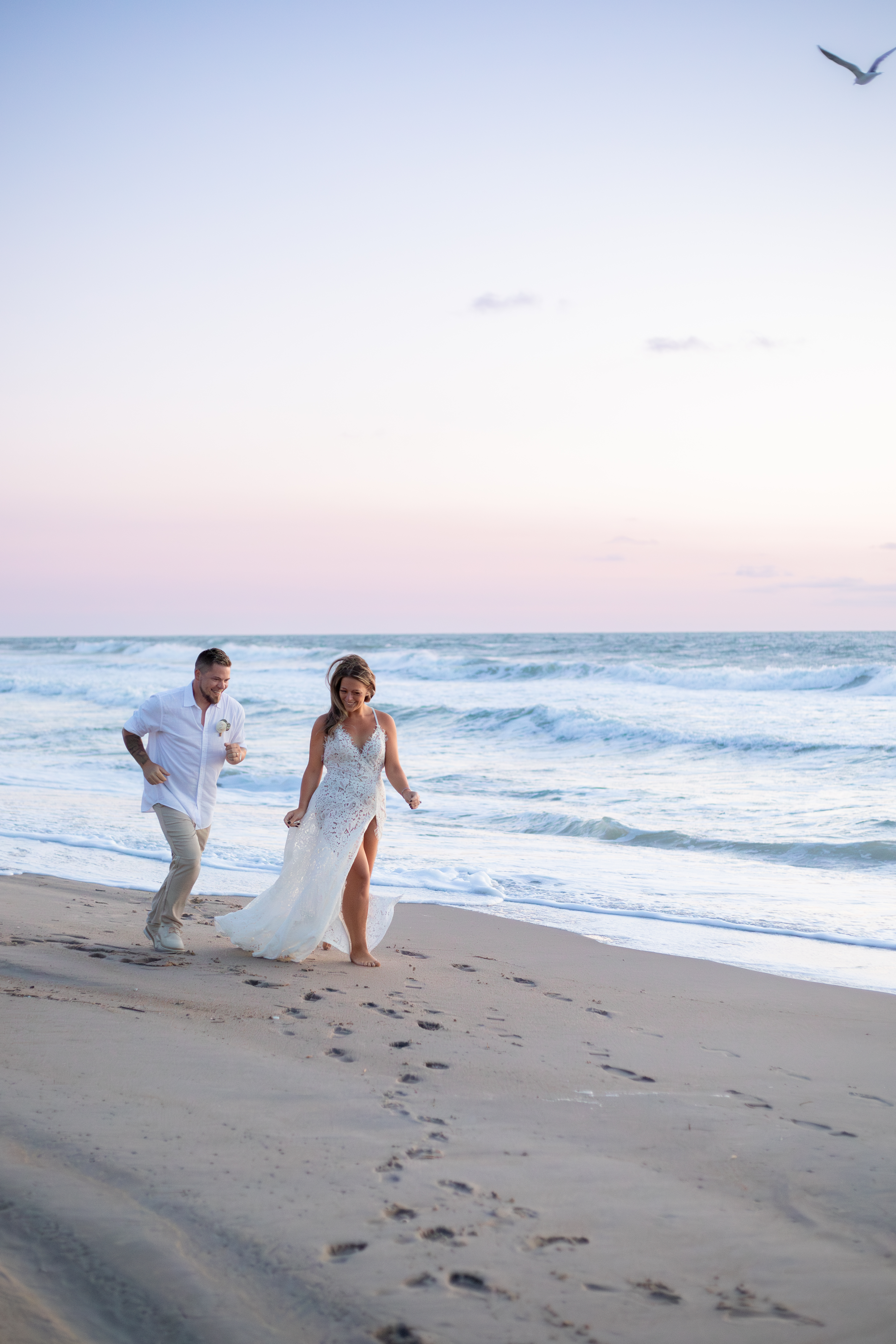 Couple running and laughing on a Virginia Beach shoreline at sunset with pink and purple sky