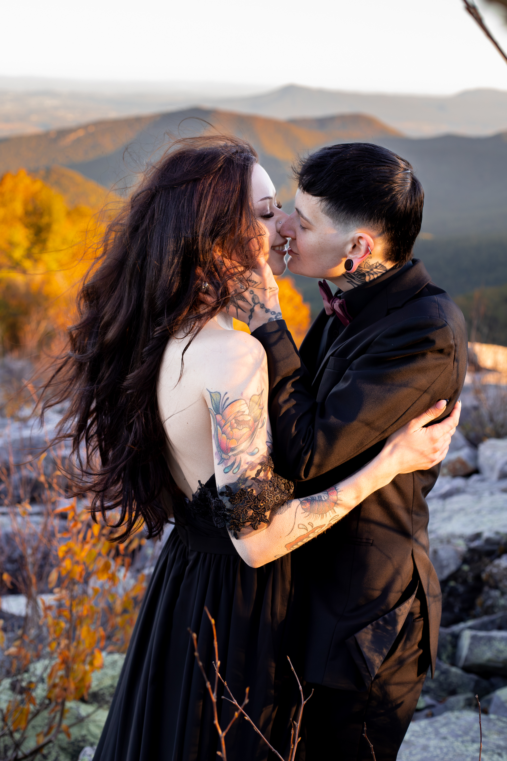 Couple kissing at Blackrock Summit in Shenandoah at golden hour with orange and gold fall foliage and mountain valley views behind them