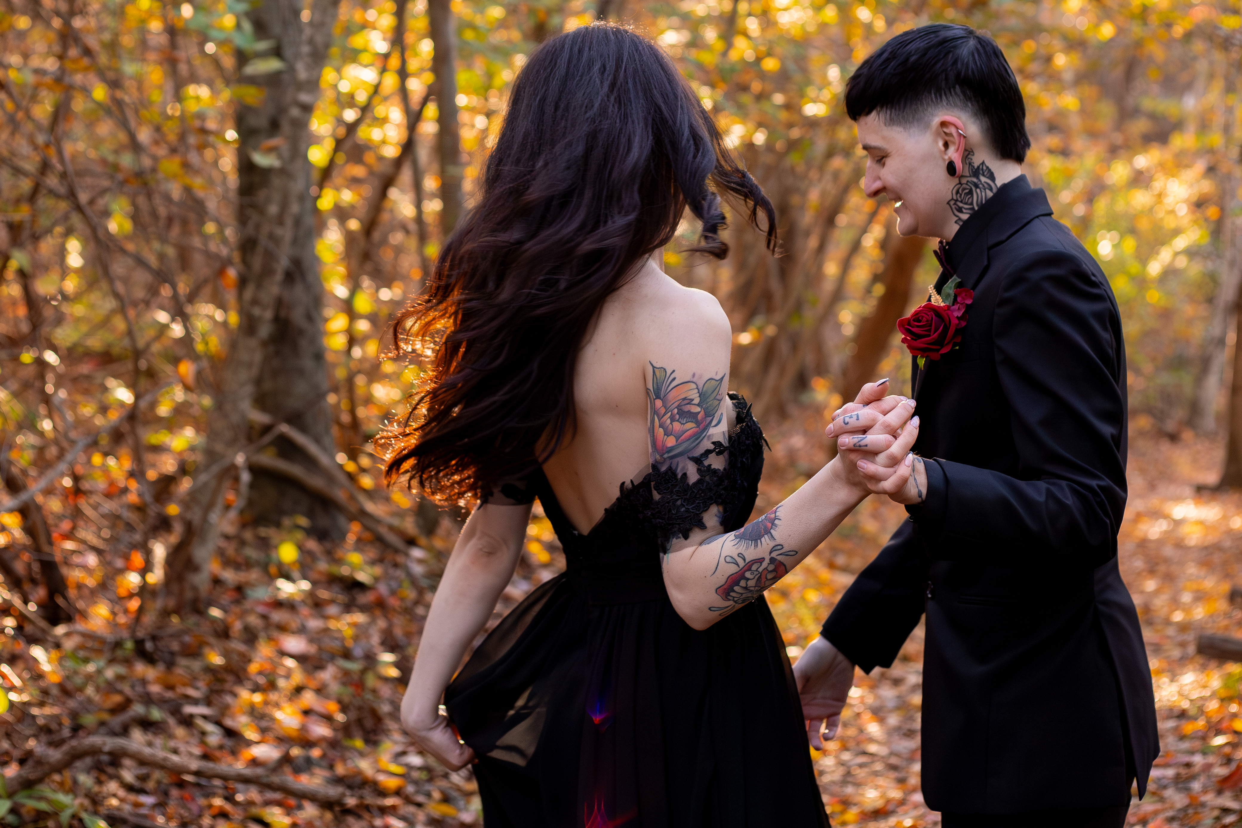 Couple in matching black outfits holding hands in a Shenandoah forest at peak fall foliage with orange and golden leaves all around them