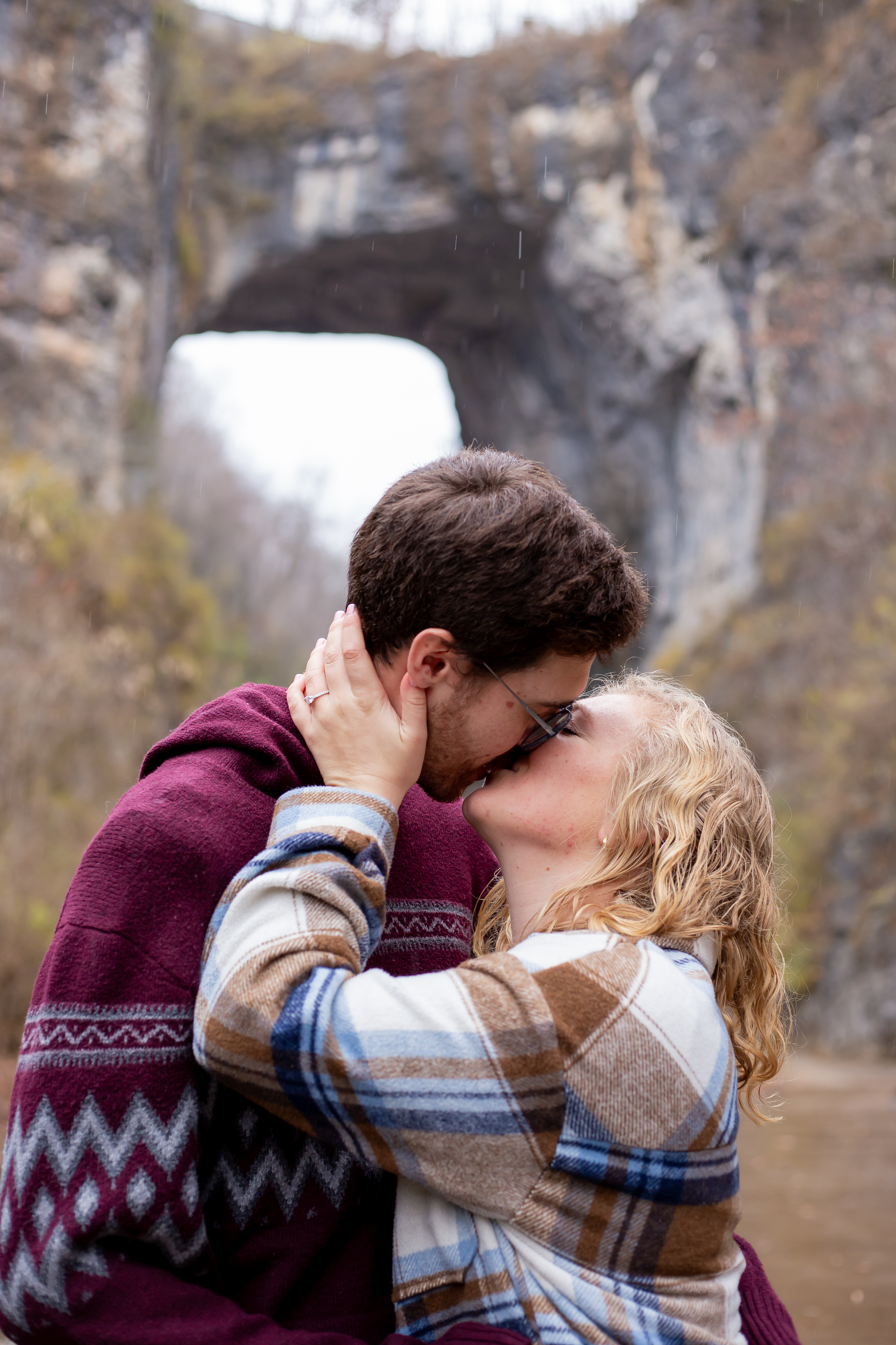 Couple kissing in front of the Natural Bridge limestone arch in Virginia, rain falling around them